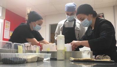 Elodie apprend à Ataullah, réfugié afghan et Hadil, réfugiée syrienne, à dresser les assiettes à la manière française.